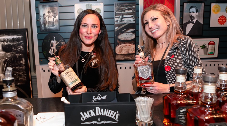 2 women holding different types of whiskey bottles